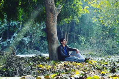 Teenager sitting besides tree trunk in forest