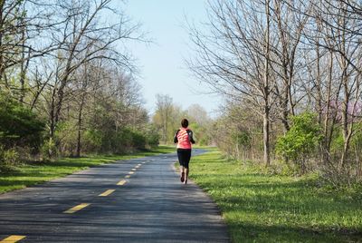 Rear view of woman running on road amidst bare trees