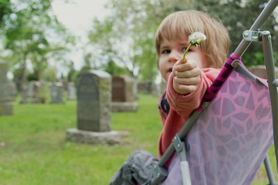 Baby boy holding flower while sitting on stroller at cemetery