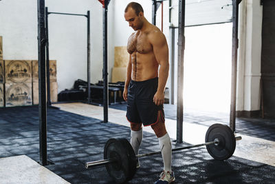 Full length of shirtless young man with barbell in gym