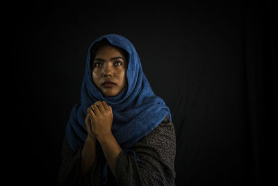 Portrait of young man sitting against black background