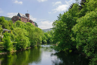 Scenic view of river amidst trees and buildings against sky