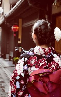 Rear view of young woman in kimono standing on road against house