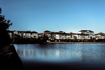 Buildings by river against blue sky
