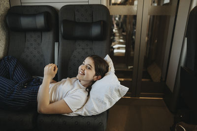Smiling girl lying on seat while traveling in train
