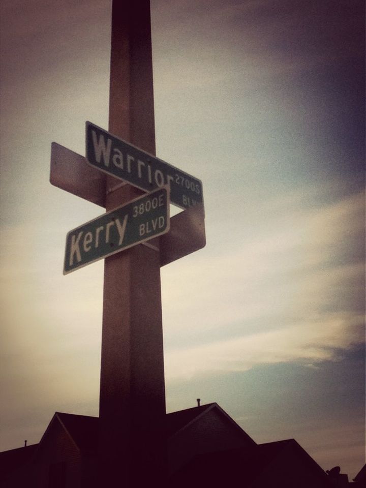 text, communication, low angle view, built structure, architecture, guidance, western script, building exterior, sky, sign, information sign, direction, road sign, sunset, information, directional sign, non-western script, arrow symbol, cloud - sky, city