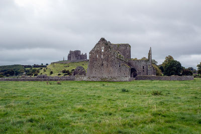 Old ruin building on field against cloudy sky