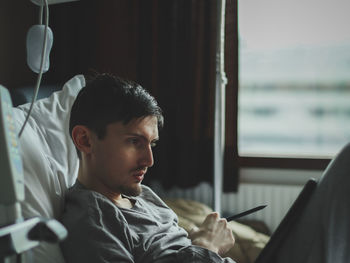 Young man patient with a tablet lying in the hospital ward.