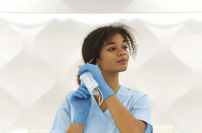 Portrait of smiling young woman standing against white wall