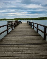 Wooden jetty leading to pier over sea against sky