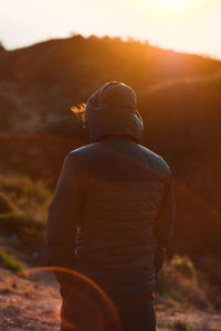 Rear view of man standing on field against sky during sunset