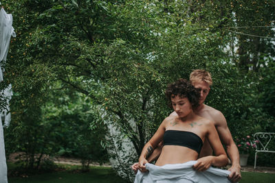 Young couple sitting on tree against plants