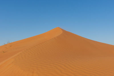 Sand dunes in desert against clear blue sky