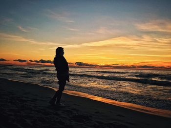 Silhouette woman standing on beach against sky during sunset