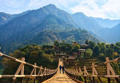 Rear view of men on footbridge against mountain