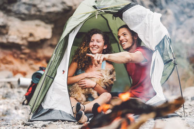 Smiling friends looking away while sitting in tent on land