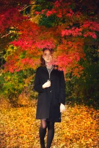 Full length of young woman standing by plants during autumn