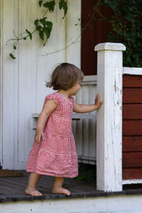 Cute girl pushing wooden railing while standing outside house