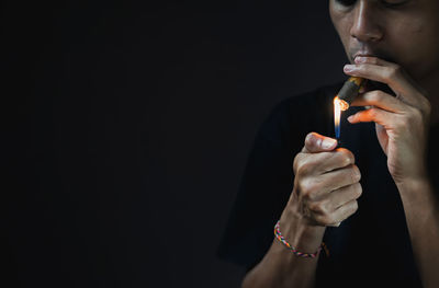 Midsection of woman holding cigarette against black background