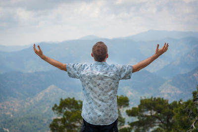 Rear view of man with arms outstretched against mountain range