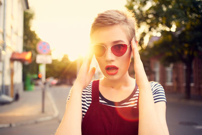 Portrait of young woman wearing sunglasses standing on street in city