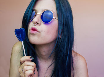 Young woman wearing blue sunglasses holding heart shape candy