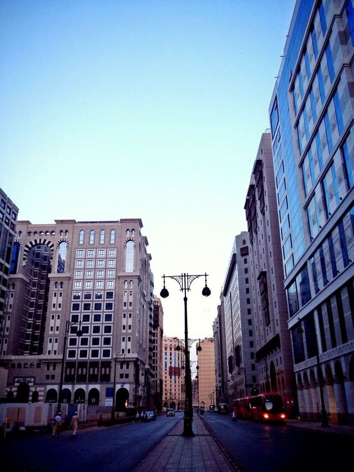 building exterior, architecture, built structure, clear sky, city, copy space, street, transportation, building, road, blue, car, city life, the way forward, diminishing perspective, city street, incidental people, outdoors, day, street light