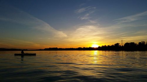 Silhouette man in lake against sky during sunset