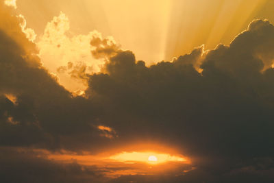 Low angle view of sunlight streaming through clouds during sunset