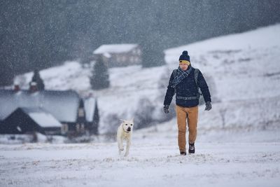 Side view of man playing with dog on field during snowfall