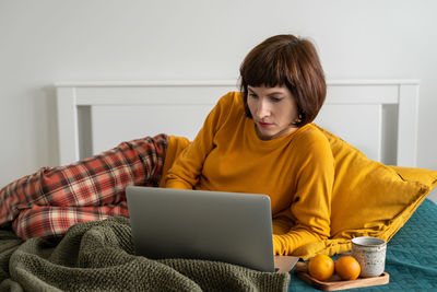 Smiling woman using laptop while sitting on bed at home