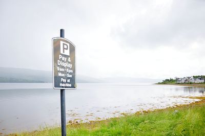 Information sign by lake against sky