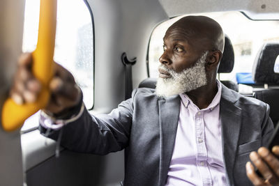 Senior businessman holding handle and looking through taxi window