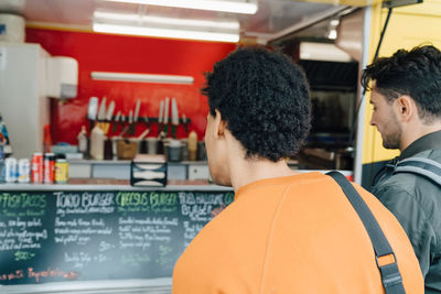 Rear view of male friends looking at menu of food truck in city