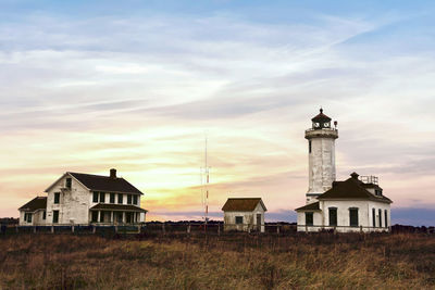 Lighthouse by building against sky at sunset