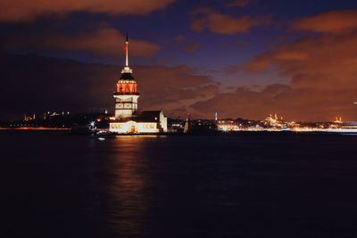 Illuminated building by sea against sky at night