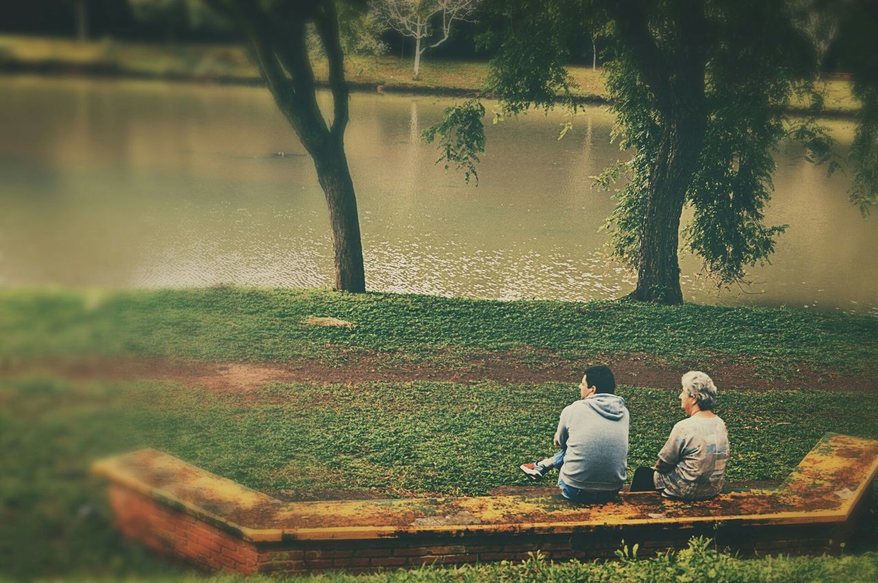 lifestyles, leisure activity, water, sitting, childhood, tree, casual clothing, full length, lake, grass, bench, relaxation, girls, boys, elementary age, nature, rear view, park - man made space