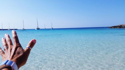 Close-up of hands against sea against clear sky