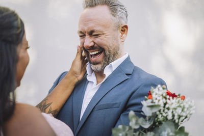 Mature groom laughing while looking at bride against wall