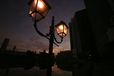 Illuminated lamppost by river in city at dusk