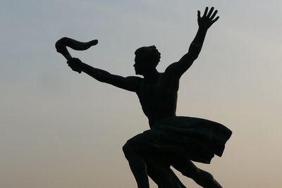 Low angle view of silhouette man statue against sky during sunset