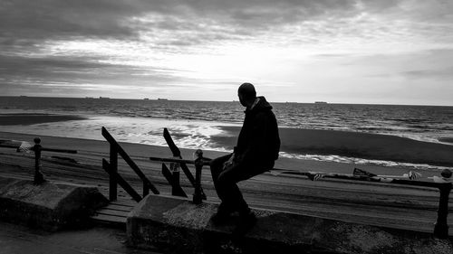 Man sitting on bench while looking at sea against sky
