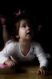 Cute girl looking up while lying on hardwood floor in darkroom