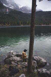 Man standing on rock by lake against sky