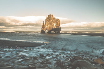 View of rocks in sea against cloudy sky