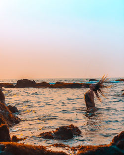 Man surfing in sea against sky during sunset