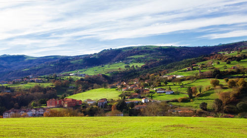 Scenic view of green landscape and houses against sky