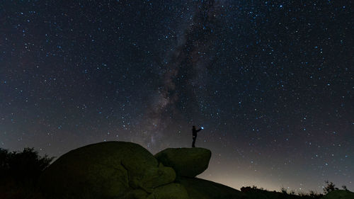 Low angle view of silhouette man standing on rock against star field