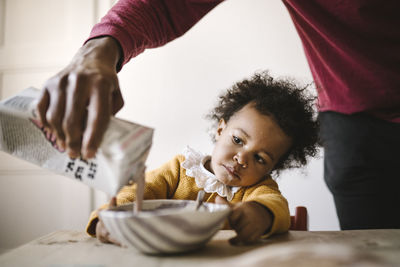 Girl watching father pour milk into bowl