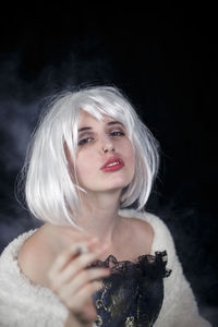 Portrait of female model smoking cigarette against black background